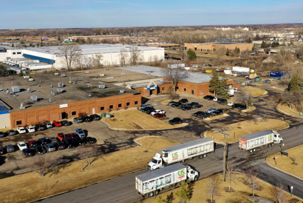Drone picture of the Knowledge Computers commercial space from 200 feet in the air. In the foreground, three semi-trucks. The building is brick and there is a large parking lot in front with numerous cars.
