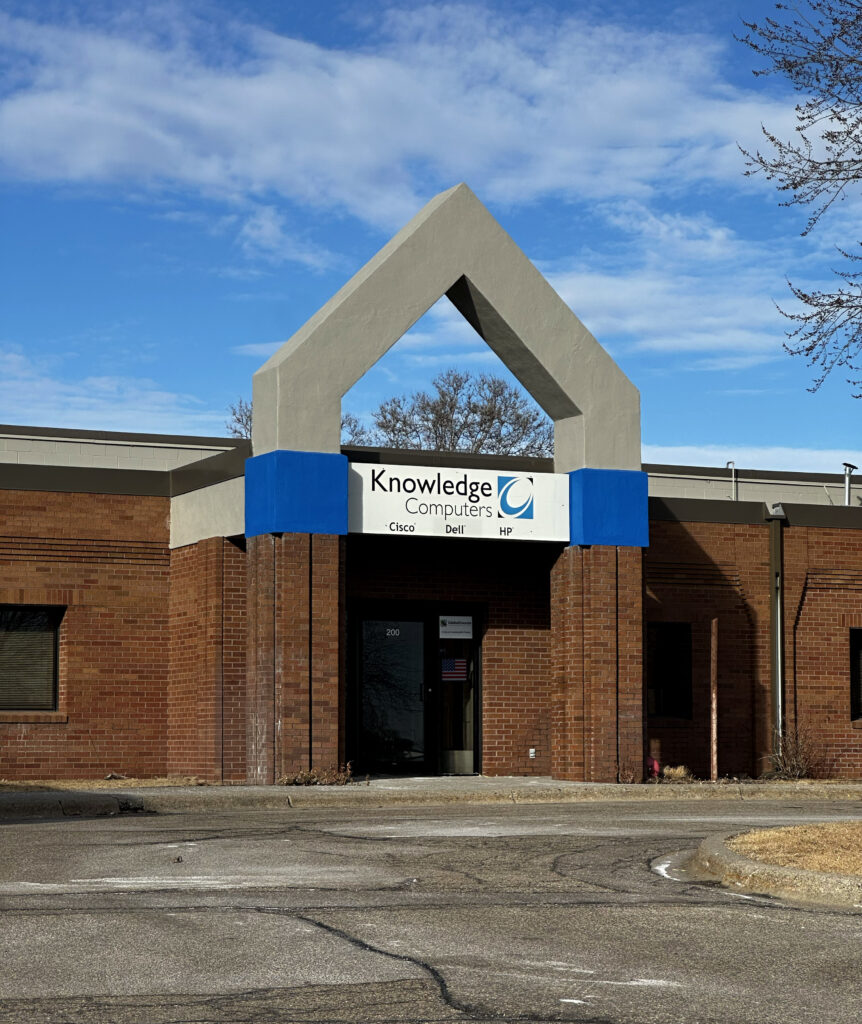 IMG_8883_E A picture of Knowledge Computers store. a red brick building with a concrete triangle above the door and a sign that reads Knowledge Computers.